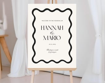 May include: A white wedding welcome sign with a black wavy border. The sign reads "Welcome to the wedding of Hannah & Mario 10.11.2025" and "Thank you so much for joining us".