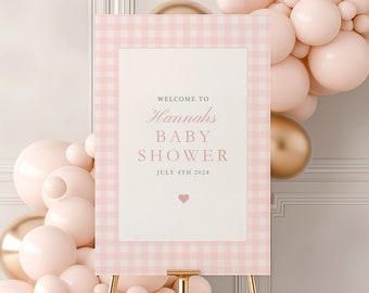 Op de afbeelding: Een roze en wit gingham baby shower welkomstbord met de tekst "Welkom op Hannah's Baby Shower 4 juli 2024" en een klein roze hartje.