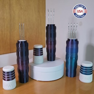 May include: A collection of dark purple and blue needle holders with silver needles, and matching white and purple containers. The containers have the text "ordWr" on them. The image also includes a "Proudly Made in USA" sticker.