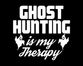 May include: White text on a black background reads "Ghost Hunting is my Therapy" with two white ghost silhouettes on either side of the text.