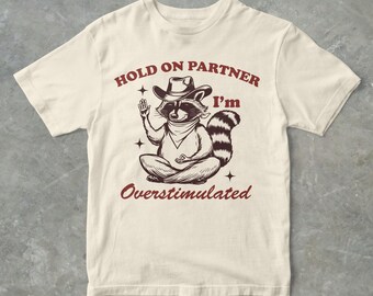Hold On Partner I'm Overstimulated Lustiges Cowboy-Waschbär-Grafik-T-Shirt, Unisex-T-Shirt für Erwachsene, Geschenk für Sie, Geschenk für Ihn, Waschbär-T-Shirt