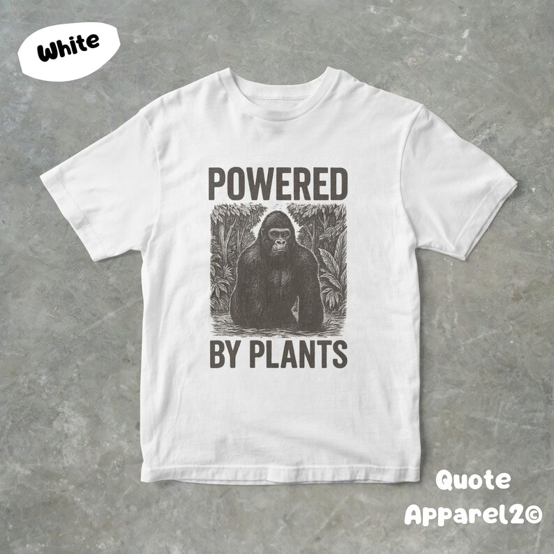 May include: White t-shirt with a black and white graphic of a gorilla in a jungle setting. The text "POWERED BY PLANTS" is above and below the gorilla image. The shirt is from Quote Apparel2O.