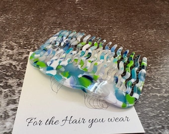 May include: A hair comb featuring a wavy, multi-colored pattern of blue, green, and white acrylic. The comb rests on a white display card with a line drawing of a head and the printed text, For the Hair you wear, in a black script font.
