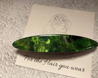 May include: Green and black marbled resin hair clip. The clip is oval shaped and has a glossy finish. The text "For the Hair you wear" is printed on the white background.