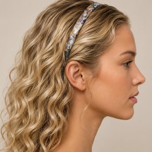 May include: A thin headband featuring a multi-colored tortoiseshell pattern with shades of grey, white, brown, and hints of blue. The accessory has a smooth, polished finish and a rounded profile, designed to sit securely across the top of the head.
