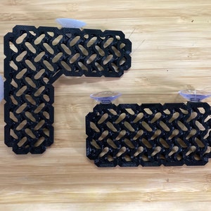 Peut inclure: Deux étagères noires à motifs géométriques avec ventouses. L'une est en forme de L, l'autre est rectangulaire. Les étagères sont faites d'un matériau sombre et sont conçues pour être montées sur une surface lisse.