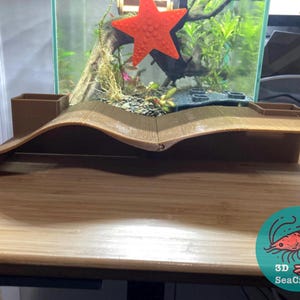 May include: A curved wooden bridge for a fish tank, with a small brown planter on each side. The bridge is made of multiple pieces of wood that are joined together. The bridge is sitting on a wooden surface. The image also includes a logo for 3D SeaCrafts.