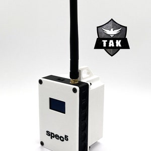 May include: A white wireless receiver with a black antenna and a small screen. The receiver has the text "spec5" printed on the front. The receiver is sitting on a white surface.