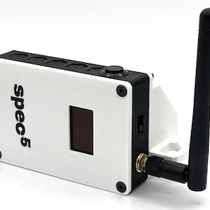 May include: A white and black wireless device with a small screen and the text "spec5" printed on the front. The device has a black antenna and a small black button on the top.