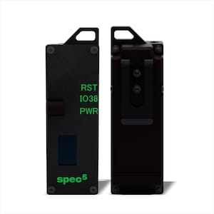 May include: A black device with a green text display that reads "RST IO38 PWR" and "spec5". The device has a black clip on the side and a small black button on the front.