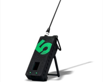 May include: A black and green handheld radio transmitter with a long antenna. The radio has a small screen and a number "5" printed on the front. The radio is on a stand.