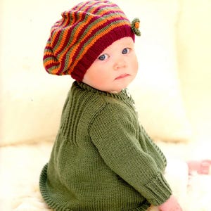 Peut inclure: Un bébé portant un pull vert tricoté et un béret rayé avec un petit ornement floral. Le béret présente des rayures bordeaux, orange et vertes. L'image est tirée d'un livre de tricot fait main.