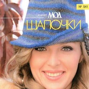 May include: A woman smiles, wearing a blue and gray knitted hat with a brim. The hat has a striped pattern. The cover of a magazine is visible, with text in a foreign language. The magazine is labeled "No. 541".