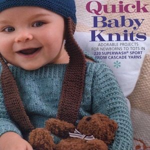 May include: A baby wearing a blue and brown knitted bear hat with ear flaps and a matching sweater. The image also shows the cover of a book titled "60 More Quick Baby Knits".