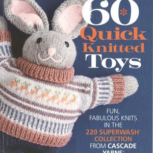 Puede incluir: Un juguete de conejo tejido con cabeza gris, orejas internas rosas y nariz rosa. El conejo lleva un suéter con patrones de zanahorias y rayas. La imagen es de un libro titulado "60 Quick Knitted Toys."