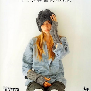May include: A woman wearing a gray knitted hat and matching fingerless gloves. The hat has a cable knit pattern. The woman is wearing a blue and white striped shirt and black pants. The text "love knit" is printed in a white box with a red heart. The text "この本の使用糸が 通信販売で買えます" is printed in black below the box. The text "ONDORI" is printed in black at the bottom of the image.