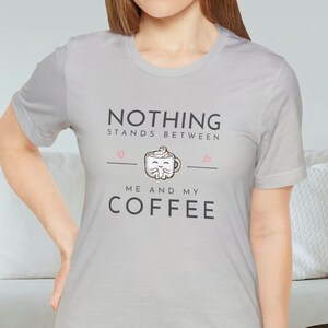 May include: A light gray t-shirt with a graphic print that says "Nothing stands between me and my coffee" with a cartoon coffee cup with a cat face.