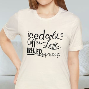 May include: A white t-shirt with black text that reads "iced cold coffee latte brewed espresso".