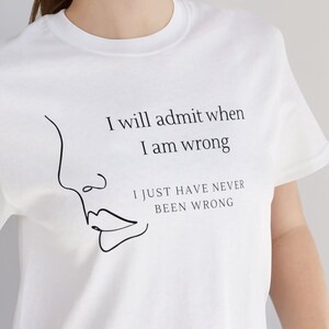 May include: White t-shirt with a black line drawing of a face and the text "I will admit when I am wrong I just have never been wrong."