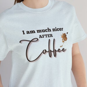 May include: A light blue t-shirt with the text "I am much nicer after coffee" in black lettering. A brown coffee stain is visible on the shirt.