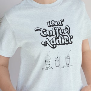 May include: A light blue t-shirt with the text "Iced Coffee Addict" in a retro font. The shirt also features a graphic of three iced coffee drinks.