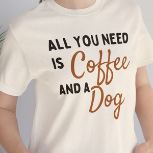 May include: White t-shirt with the text "All you need is coffee and a dog" in black and brown lettering.