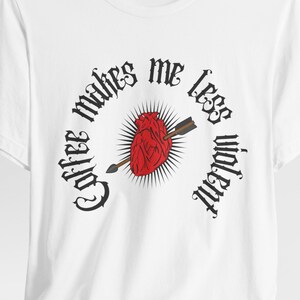 Peut inclure: T-shirt blanc avec un graphique d'un cœur rouge percé d'une flèche et le texte "Coffee makes me less violent" en police gothique.