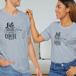 May include: Two people wearing light gray t-shirts with the text "Life Begins After Coffee" and a cartoon coffee bean holding a cup of coffee. The text is in black and the coffee bean is in gray.