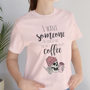 May include: Pink t-shirt with a graphic of a skeleton wearing a pink beanie and holding a coffee cup. The text on the shirt reads "I want someone to look at me the way I look at coffee."