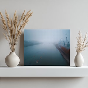 Może przedstawiać: Wydruk na płótnie przedstawiający mglistą scenę rzeczną. Obraz przedstawia rzekę z łodziami, dokiem i dźwigami. Niebo jest zachmurzone, a paleta kolorów jest stonowana z odcieniami niebieskiego, szarego i brązowego.