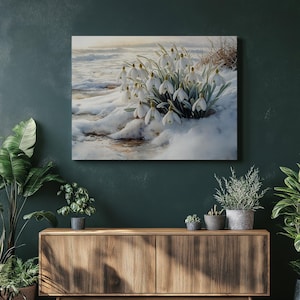 May include: A canvas print showing snowdrop flowers in a snowy scene. The image displays white flowers with green stems and leaves, set against a backdrop of snow and a soft, blurred sky. The artwork has a cool and serene colour palette.