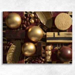 Può includere: Composizione dall'alto con sfere dorate, blocchi rettangolari e un disco strutturato, insieme a chicchi di cacao e foglie. Gli oggetti sono disposti su una superficie a motivi con tonalità bordeaux, oro e marrone.