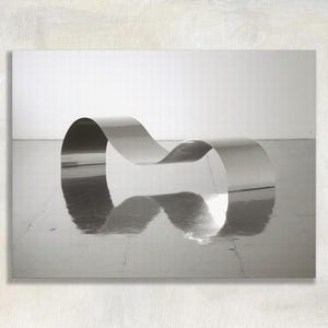 May include: A continuous, wave-shaped bench constructed from a single piece of polished, reflective silver-toned metal. The structure features smooth, flowing curves that create a serpentine form, casting a clear reflection on the floor surface.