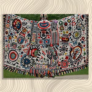 May include: A colorful, patterned textile with a central design and fringed edges. The textile features a white background with red, blue, and black geometric shapes and patterns. The design is symmetrical and intricate.