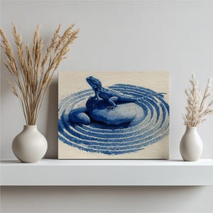 May include: A blue and white canvas print featuring a lizard on a rock in a zen garden design. The artwork has a minimalist style with a focus on the lizard and the concentric circles in the sand. The print is displayed on a white shelf.