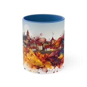 May include: A white ceramic mug with a blue rim and a colorful cityscape design. The cityscape is surrounded by abstract splashes of yellow, orange, red, purple, and blue paint.
