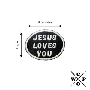 May include: Black and white embroidered iron-on patch with the text "JESUS LOVES YOU" in a white oval on a black background. The patch measures 3.75 inches wide and 3 inches tall.