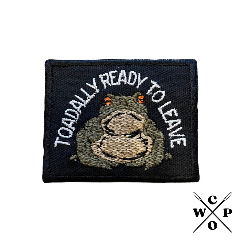 Pu&ograve; includere: Una toppa ricamata nera con un contorno bianco che presenta una rana dei cartoni animati con il testo "Toadally Ready To Leave" in bianco.