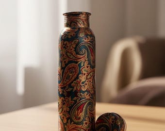 May include: A decorative water bottle with a matching cap, featuring a detailed paisley pattern in shades of teal, red, and gold. The bottle is cylindrical and sits on a wooden surface.