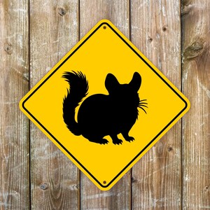 May include: A yellow diamond-shaped road sign with a black silhouette of a chinchilla. The sign has a white border and the text "Chinchilla Crossing" is not visible.