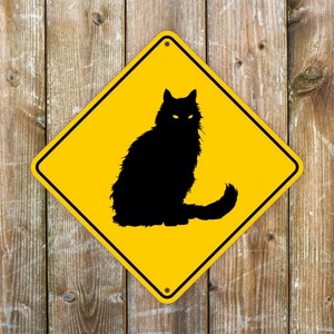 May include: A diamond-shaped yellow metal sign featuring a black silhouette of a long-haired cat with glowing yellow eyes. The sign has a black border and two small mounting holes at the top and bottom corners, centered on the vertical axis.