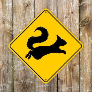 May include: Yellow diamond-shaped warning sign with a black silhouette of a squirrel running to the right. The sign has a black border.