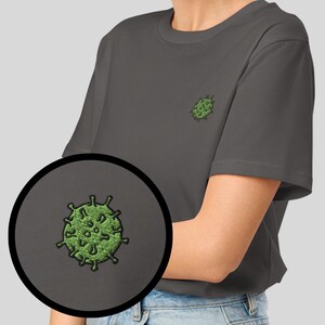 Könnte beinhalten: Dunkelgraues T-Shirt mit einem kleinen, gestickten grünen Virus-Design auf der Brust. Das Shirt ist einfarbig und hat kurze Ärmel. Eine Farbkarte der verfügbaren Shirtfarben wird angezeigt.