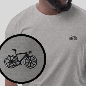 Könnte beinhalten: Ein hellgraues T-Shirt mit einem kleinen, schwarzen gestickten Bild eines Fahrrads auf der Vorderseite. Das Shirt ist in verschiedenen Farben erhältlich.