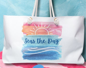 May include: White canvas tote bag with a watercolor design of a sunset over the ocean. The text "Seas the Day" is printed in blue on the bag.