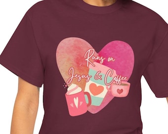 Op de afbeelding: Een maroon t-shirt met een roze aquarel hartontwerp. Het hart bevat de tekst "Runs on Jesus & Coffee".