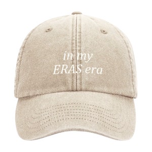 May include: A beige baseball cap with the text "in my ERAS era" embroidered in white on the front.