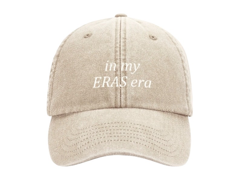 May include: A beige baseball cap with the text "in my ERAS era" embroidered in white on the front.