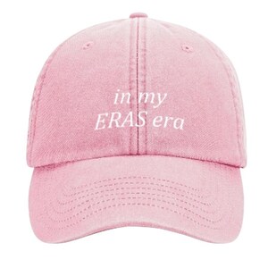May include: A pink baseball cap with the text "in my ERAS era" embroidered in white.