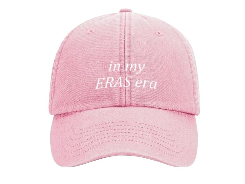 May include: A pink baseball cap with the text "in my ERAS era" embroidered in white.